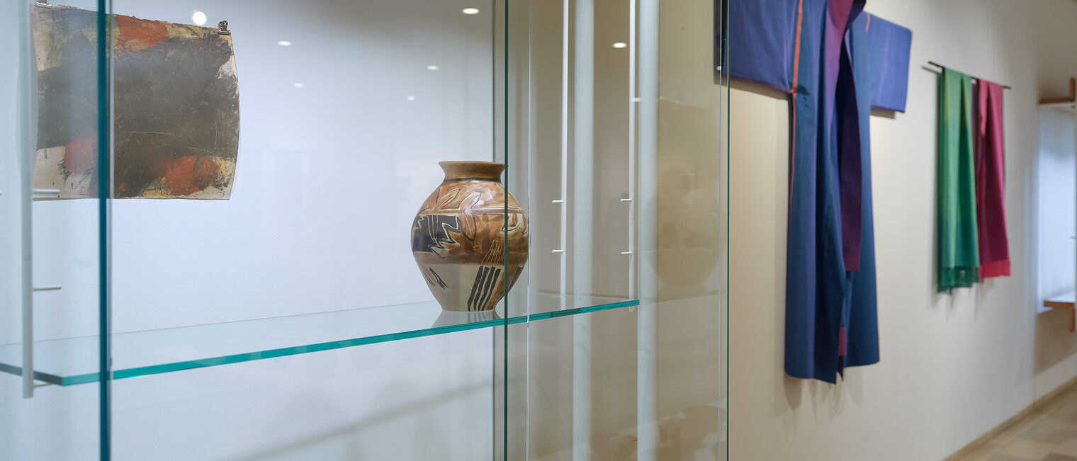 Vitrine mit Tonschalen und Vase, daneben blauer Kimono und Seidenschals an der Wand. Werke von Renate Balda und Maja Vogl.