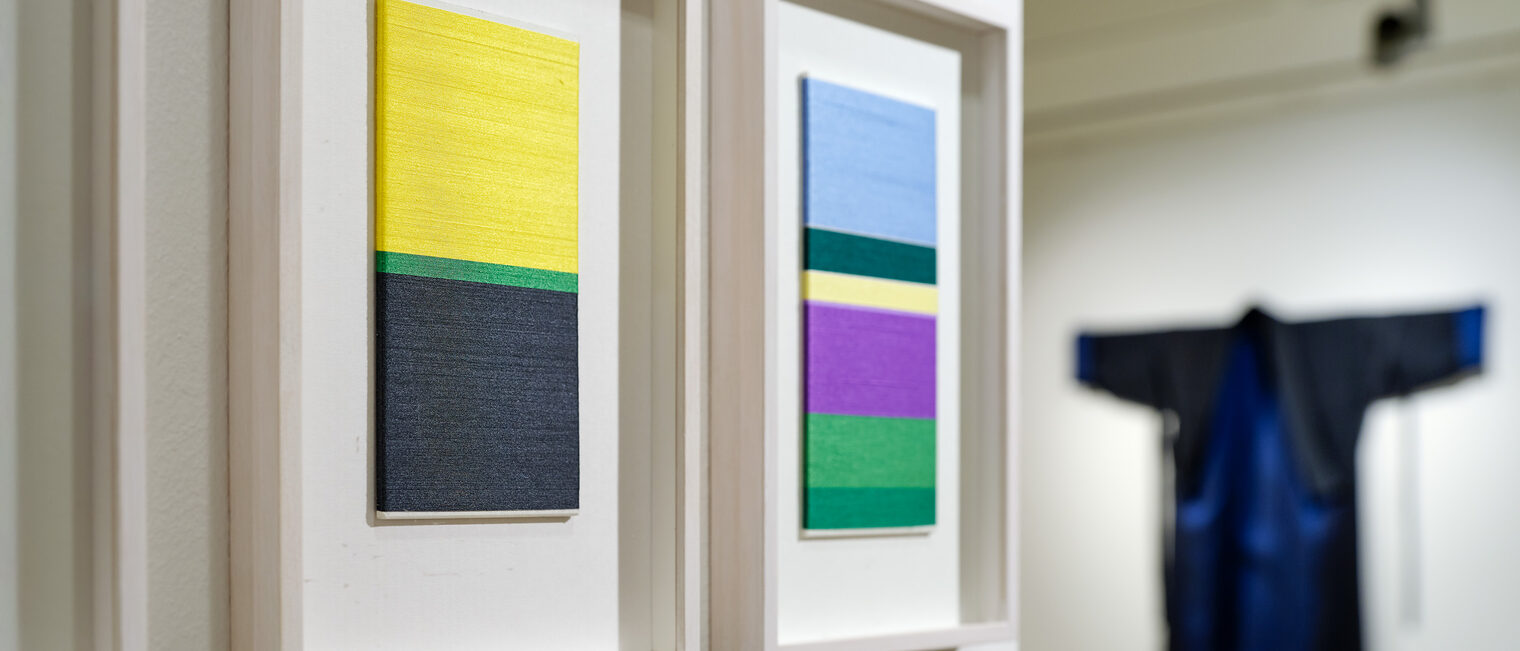 Textilkunst aus Seide der Künstlerin Maya Vogl. Im Vordergrund gerahmte Textilien mit bunten Streifen.