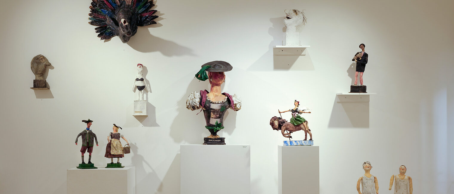 Blick auf mehrere nostalgische Figuren auf Säulen und an der Wand, teils in Tracht oder in alten Ganzkörper-Badeanzügen.