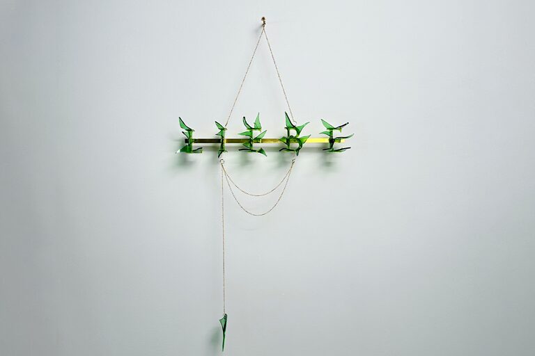 Filigraner Wandbehang mit grünen Figuren, aufgehangen an goldenen Gliederketten