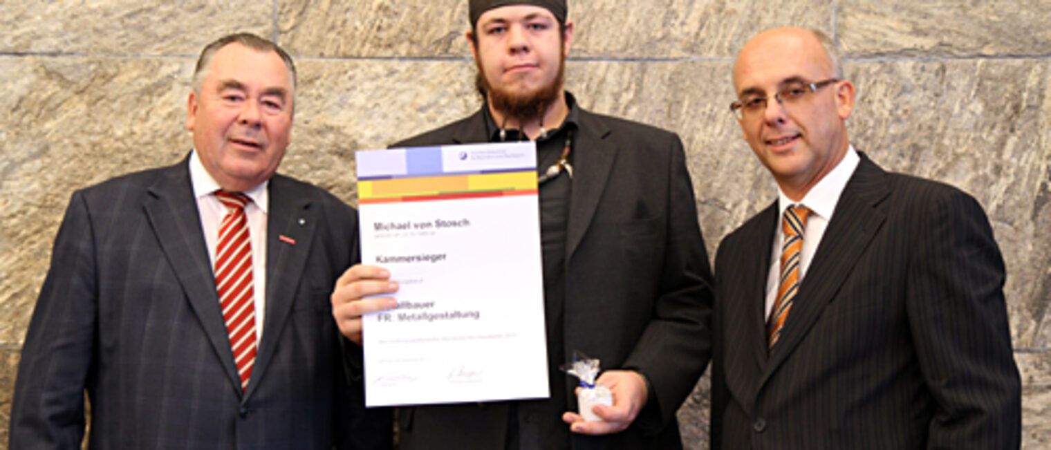 Kammerpräsident Heinrich Traublinger, MdL a. D. (links) und der Regierungsvizepräsident von Oberbayern, Ulrich Böger (rechts), gratulierten Metallbauer Michael von Stosch, Kammersieger in der Fachrichtung Metallgestaltung