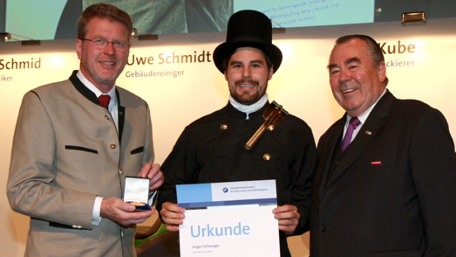 Handwerkskammerpräsident Heinrich Traublinger, MdL a. D. (rechts) und Umweltminister Dr. Marcel Huber, MdL (links) überreichten Kaminkehrermeister Jürgen Schwaiger seine Urkunde als Jahresbestmeister.